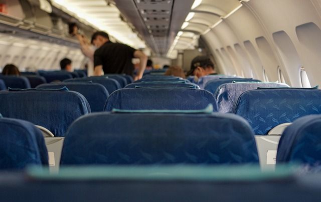 A passenger putting their bag into an open overhead bin inside an airplane cabin.