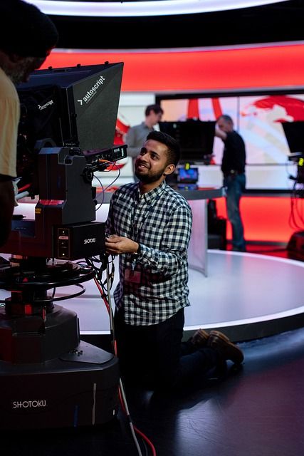A news anchor sitting in a professional television studio during a live broadcast.